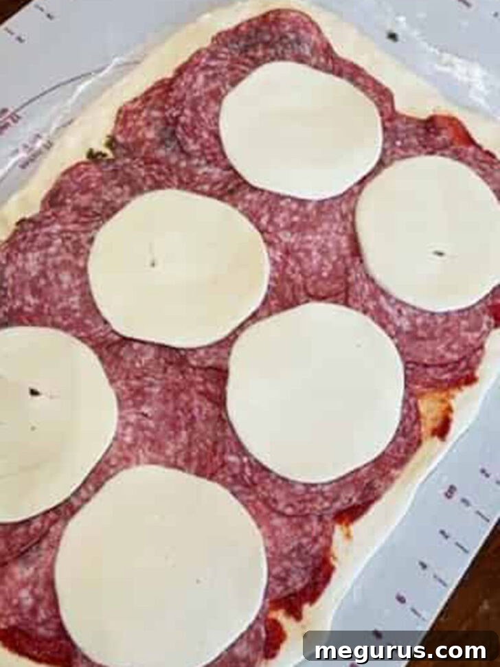Layering cold cuts and cheese generously over the stromboli dough, building the core of the filling.