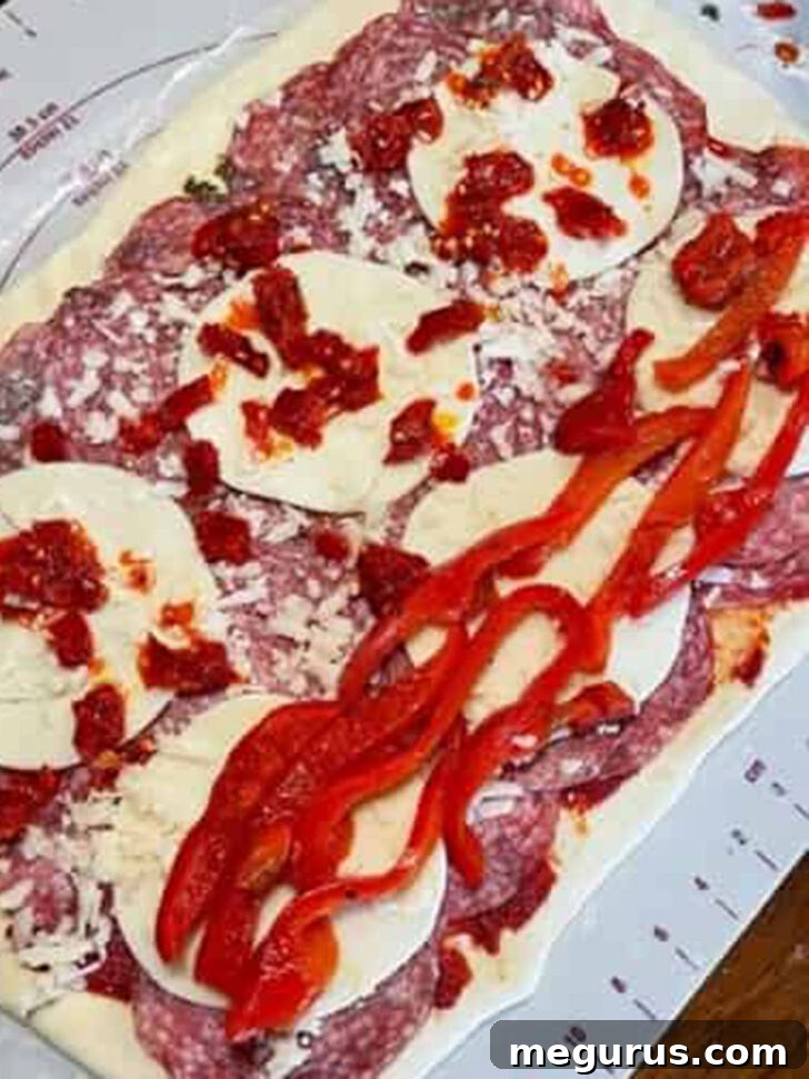 Adding colorful roasted red peppers and spicy pepperoncini on top of the meat and cheese layers.