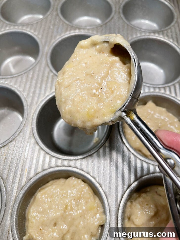Banana muffin batter being scooped into greased muffin cups.