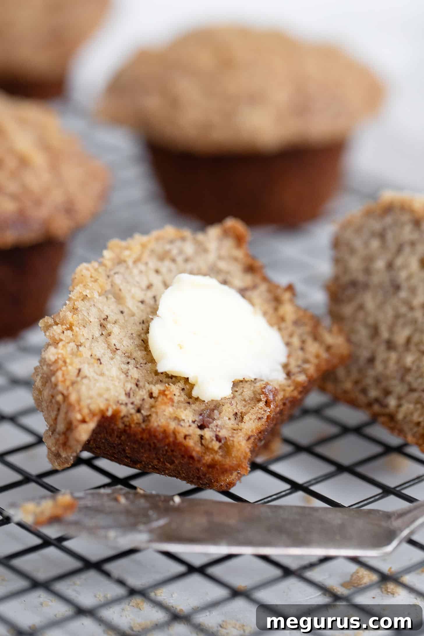 Two banana crumb muffins, split open with butter, on a cooling rack.