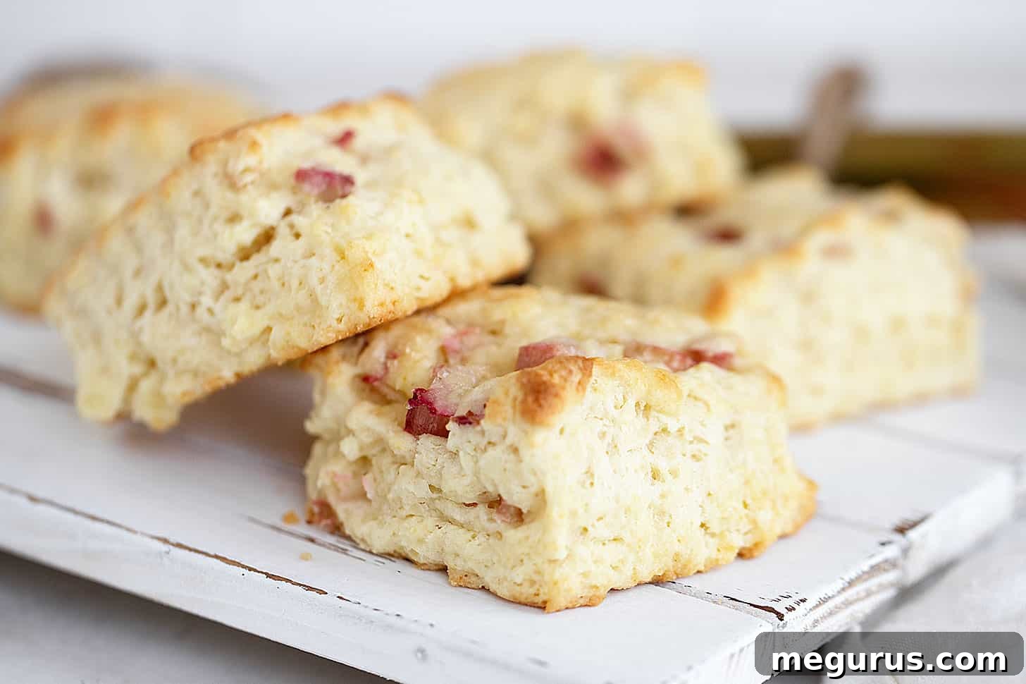 Freshly baked rhubarb scones, light golden brown with a sugary crust, arranged beautifully on a rustic wooden serving board.