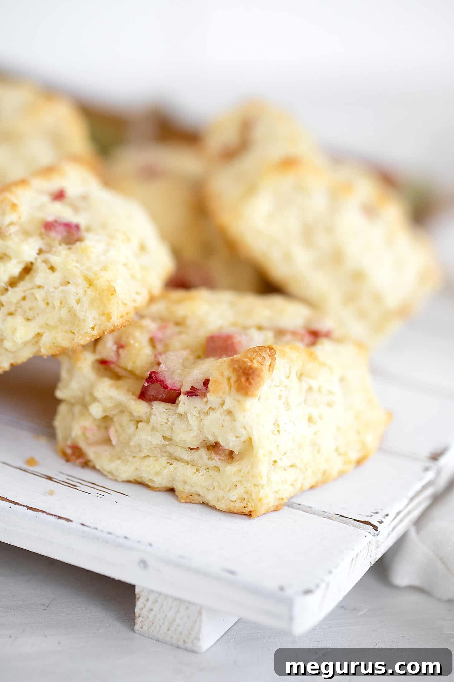 Close-up of a perfectly baked rhubarb scone on a white serving board, showcasing its flaky texture and sugary crust.