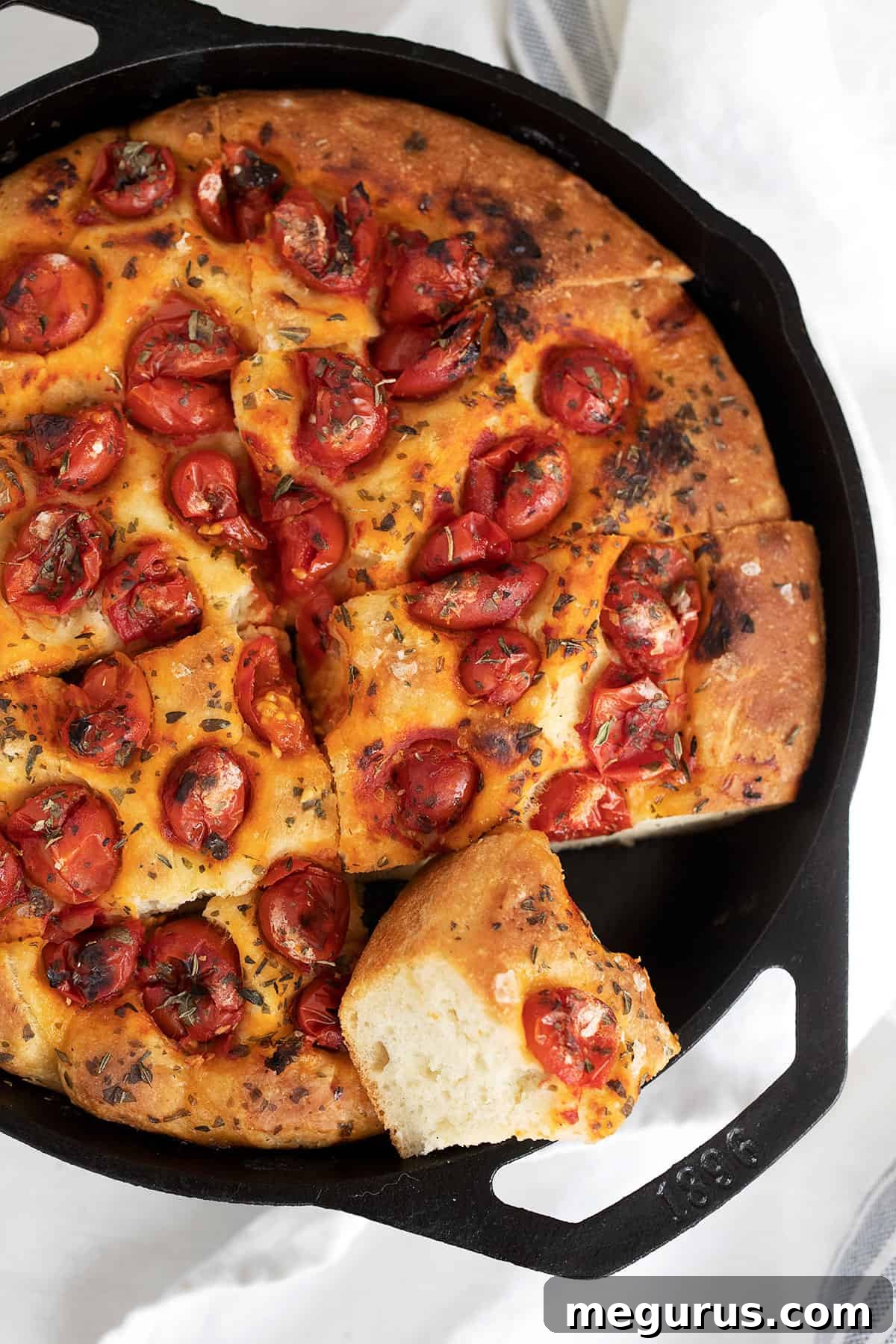 Skillet focaccia sliced in cast iron skillet, garnished with tomatoes and herbs