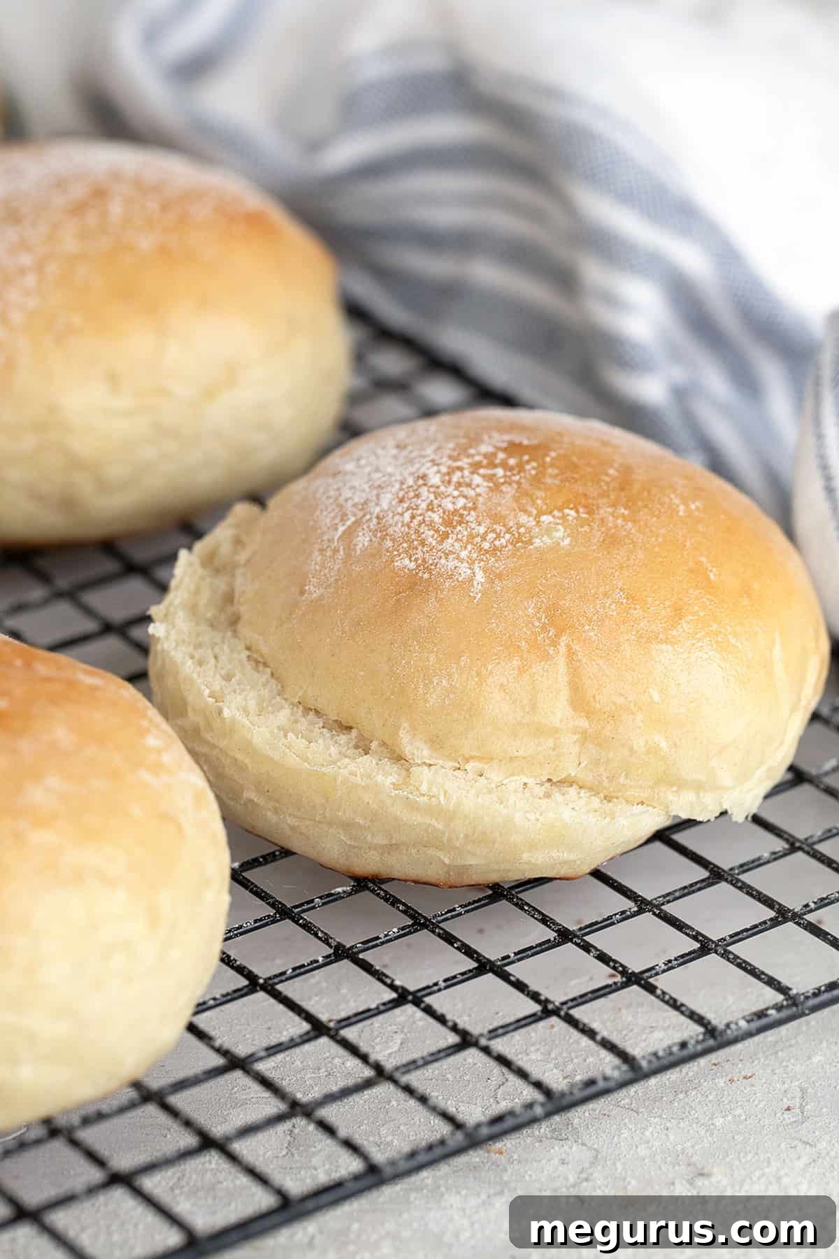 Close-up of golden brown, soft potato hamburger buns on a cooling rack, showcasing their fluffy texture.