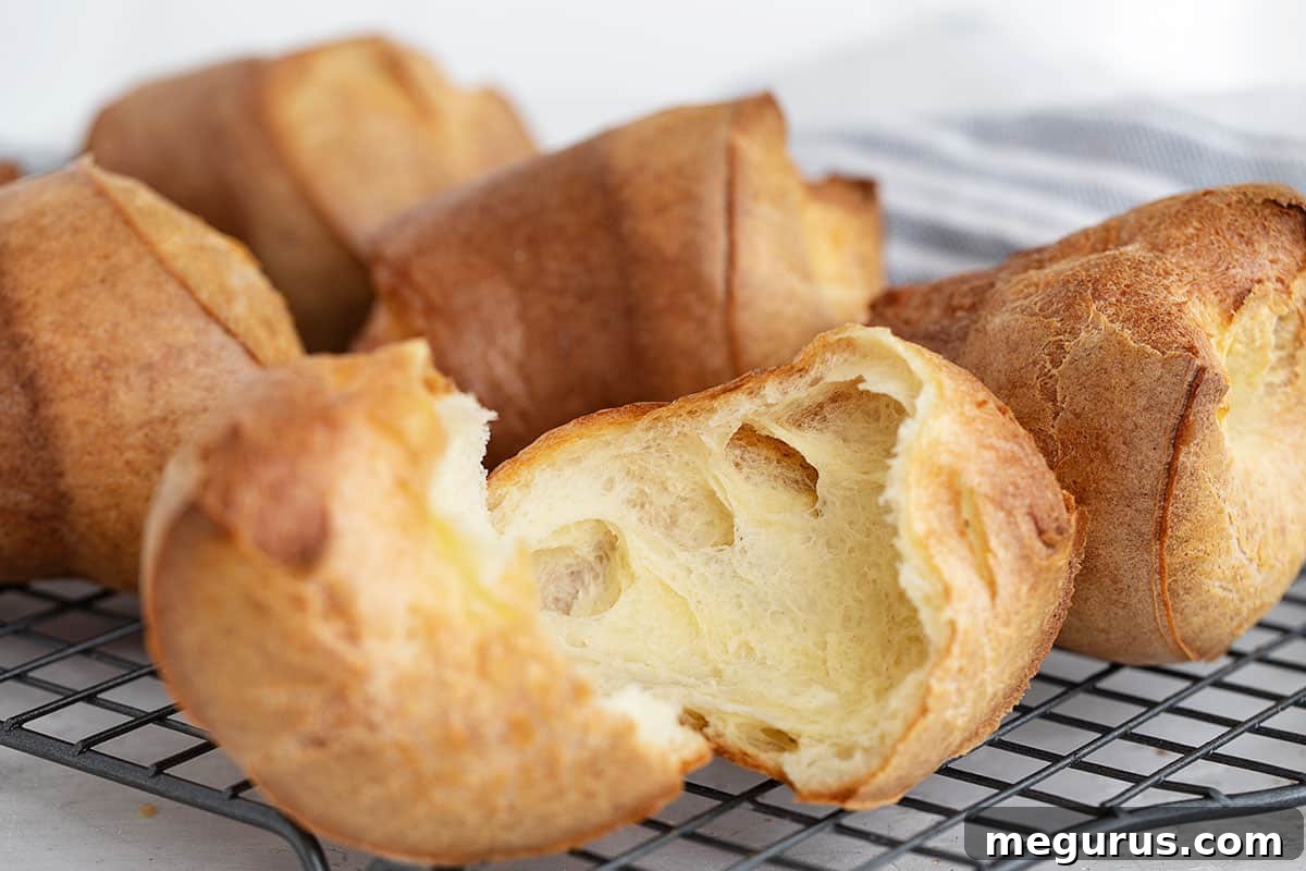 Crispy, golden popovers on a cooling rack, one split open to reveal its hollow interior