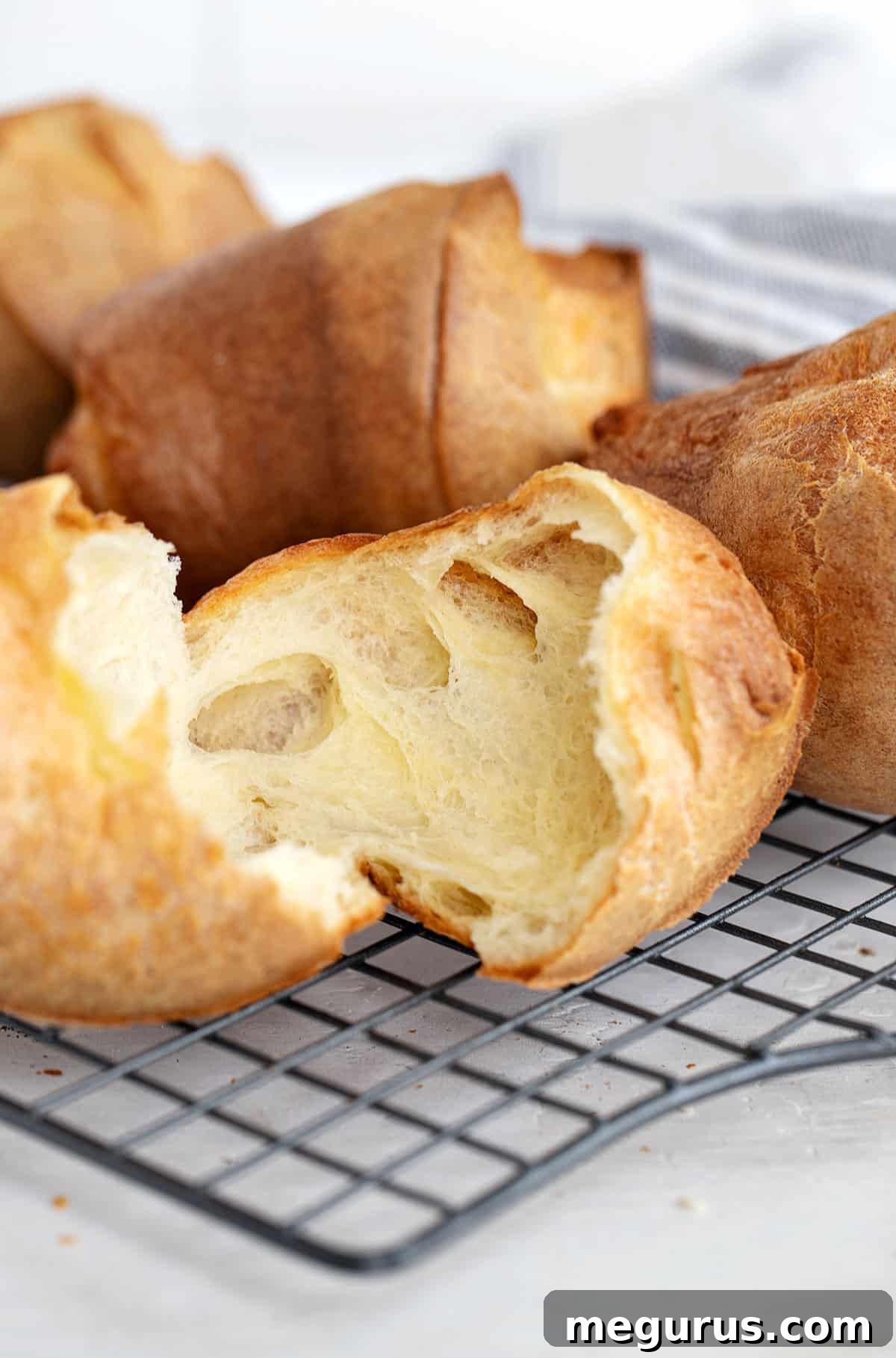 Freshly baked popovers on a cooling rack, one split open, ready to be served
