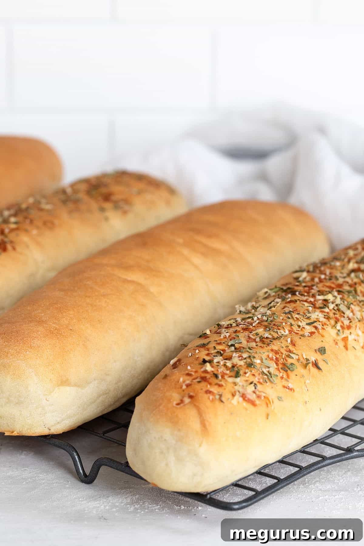 Two freshly baked sub buns resting on a wire cooling rack, ready to be filled.