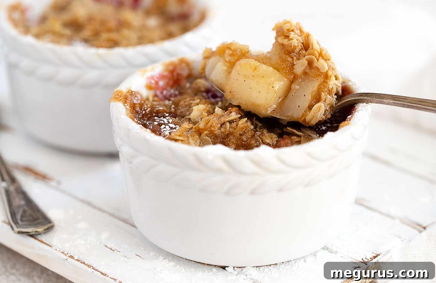 Two individual cranberry pear crisps in white ramekins, garnished with icing sugar.
