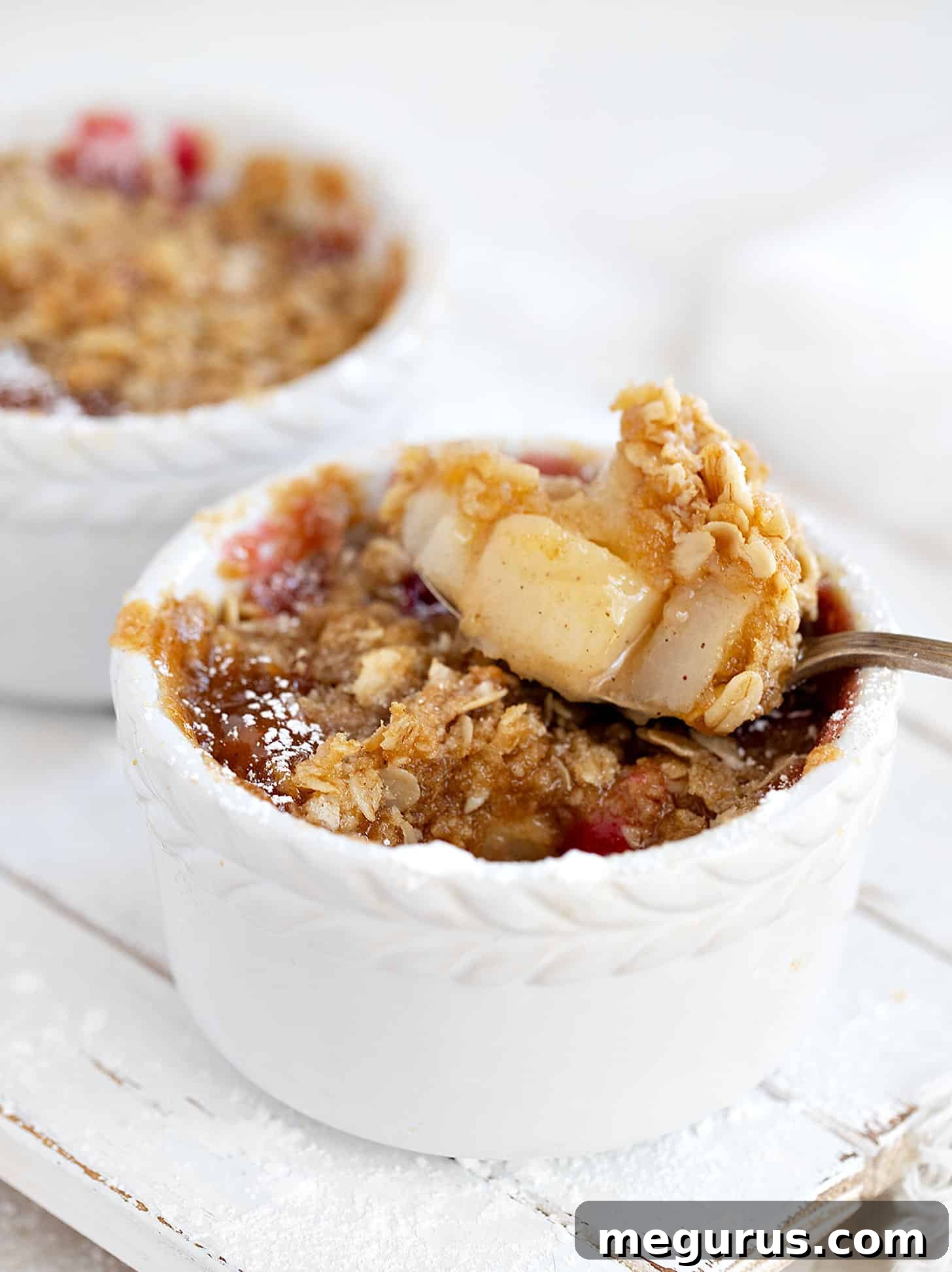 Three individual cranberry pear crisps in white ramekins on a wooden board.