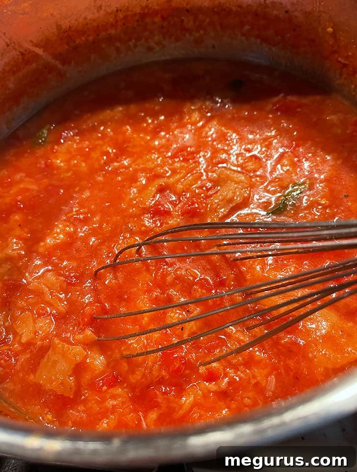 A whisk being used to break up the softened bread cubes in the tomato soup, creating a creamy texture.