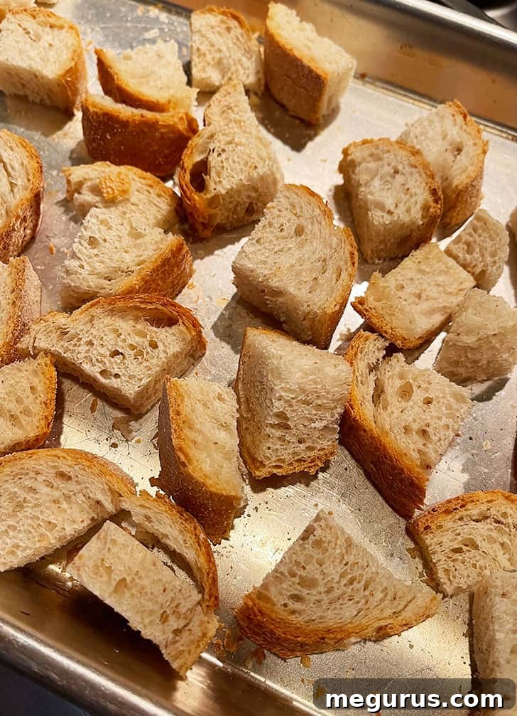 Cubed stale bread scattered on a baking sheet, ready for toasting.
