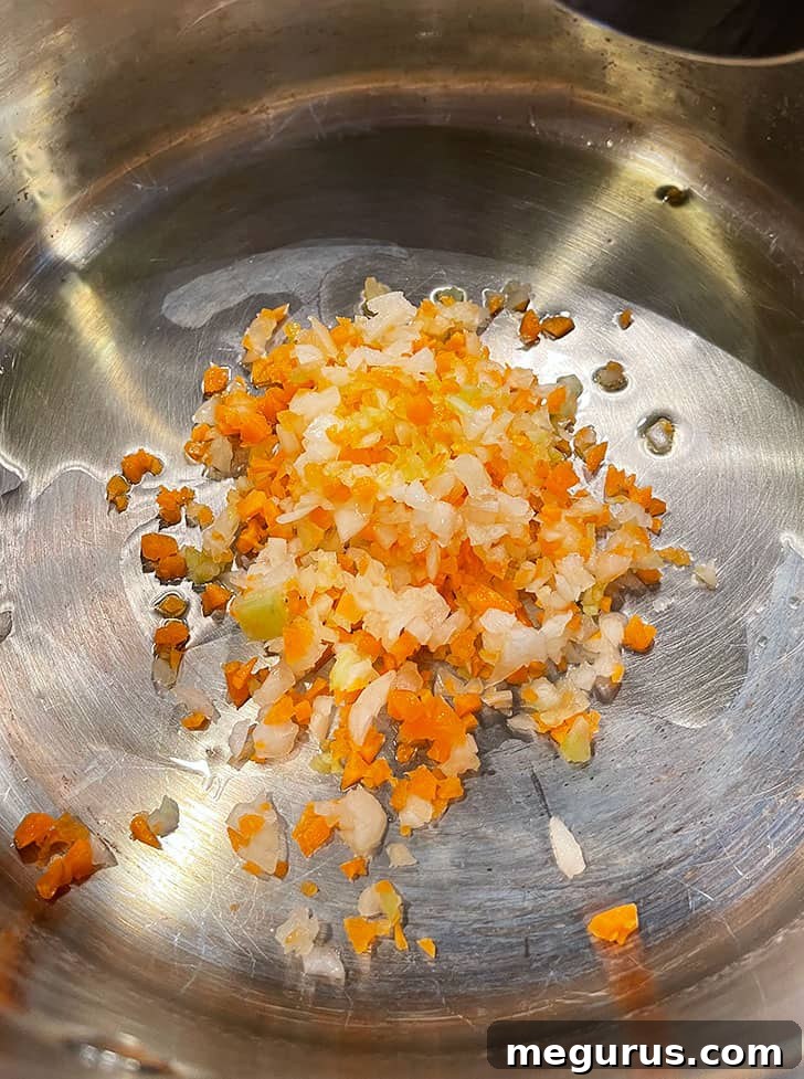 Finely diced onion, carrot, and celery being added to a pot with olive oil, beginning to sauté.