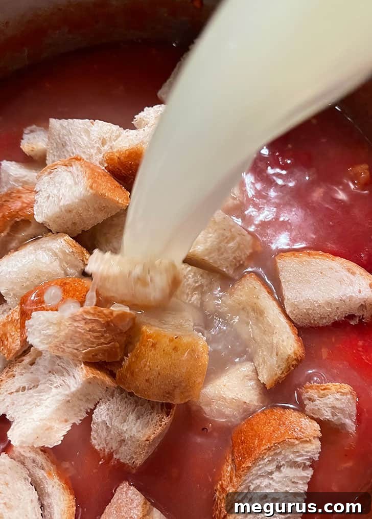 Chicken broth being poured into the pot with the tomato and bread mixture, creating the soup base.