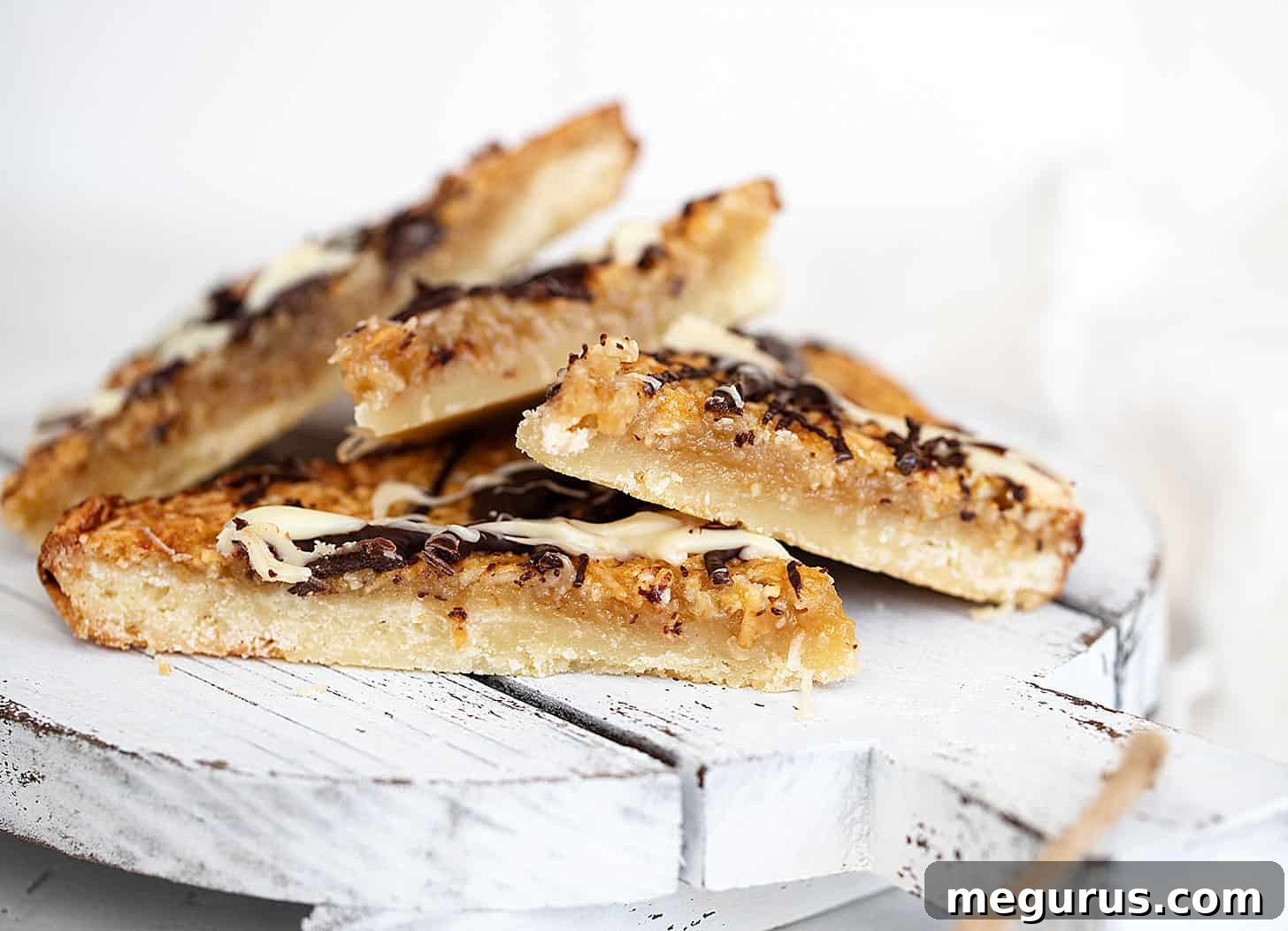 macaroon madness bars cut on white board, showcasing layers of shortbread, coconut, and chocolate drizzle.