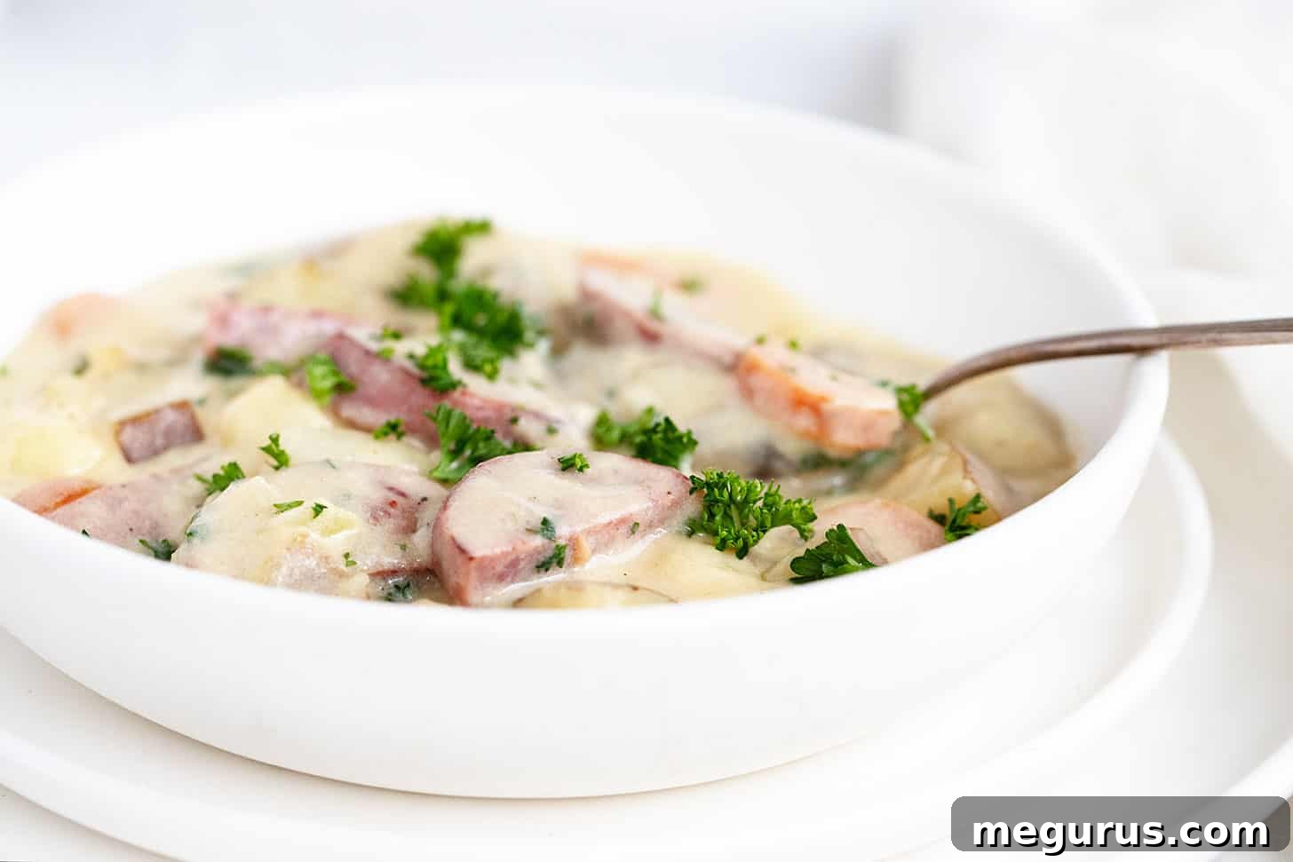 Hearty creamy potato kielbasa soup in a white bowl with a spoon, garnished with fresh parsley.