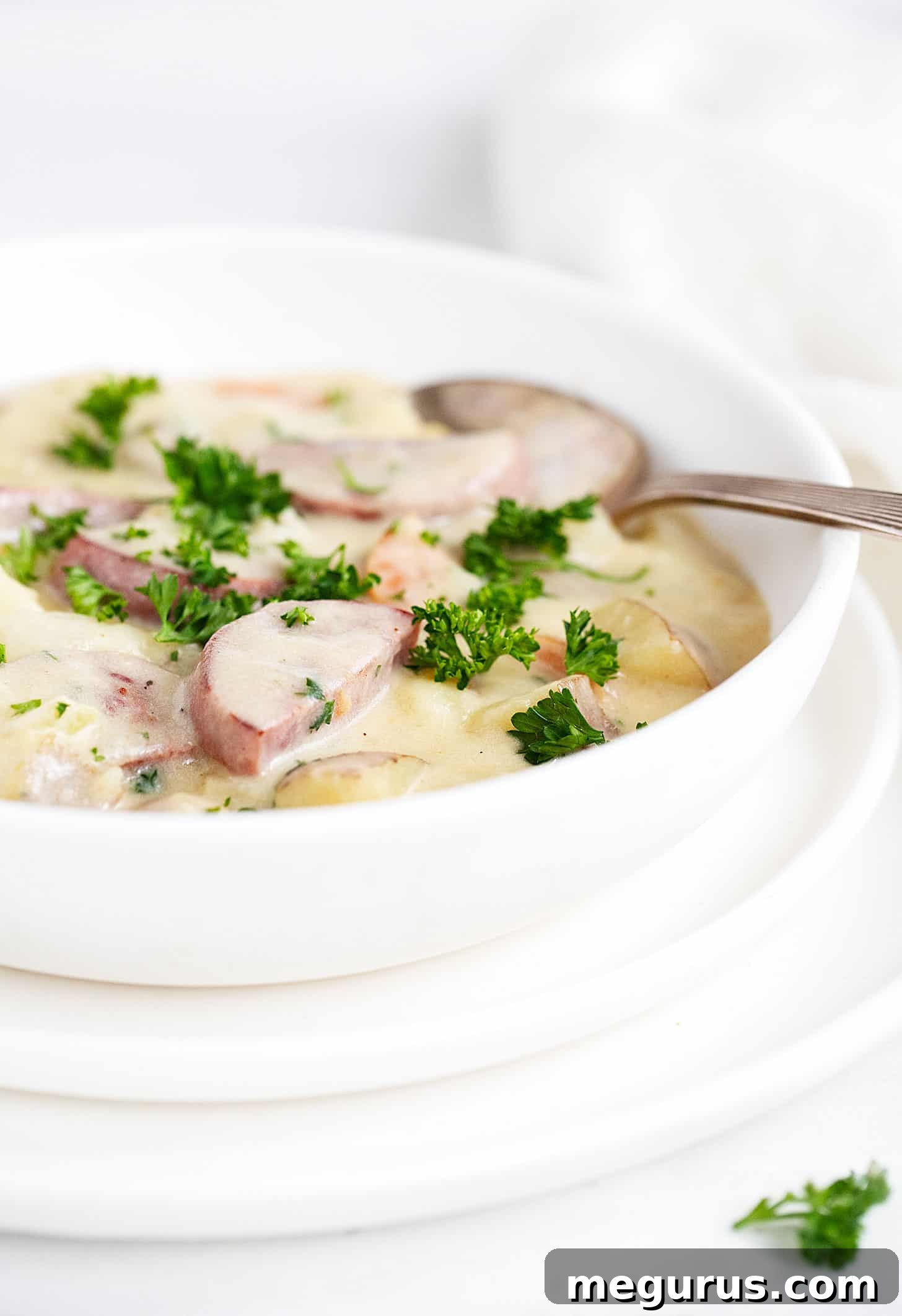 Close-up of potato kielbasa soup in a white bowl with a spoon, showing creamy texture and chunky ingredients.