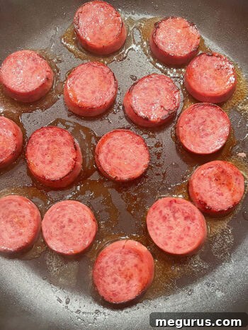 Slices of kielbasa sausage browning in a skillet.