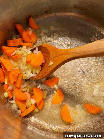 Onions and carrots sautéing in a soup pot with melted butter.
