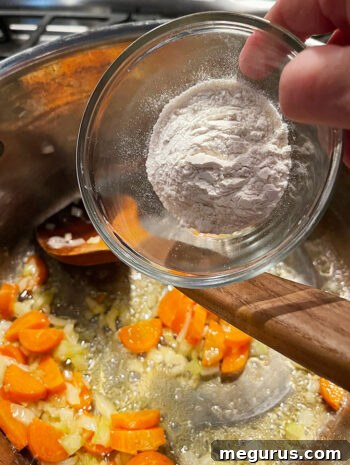 All-purpose flour being added to the sautéed vegetables in the pot.