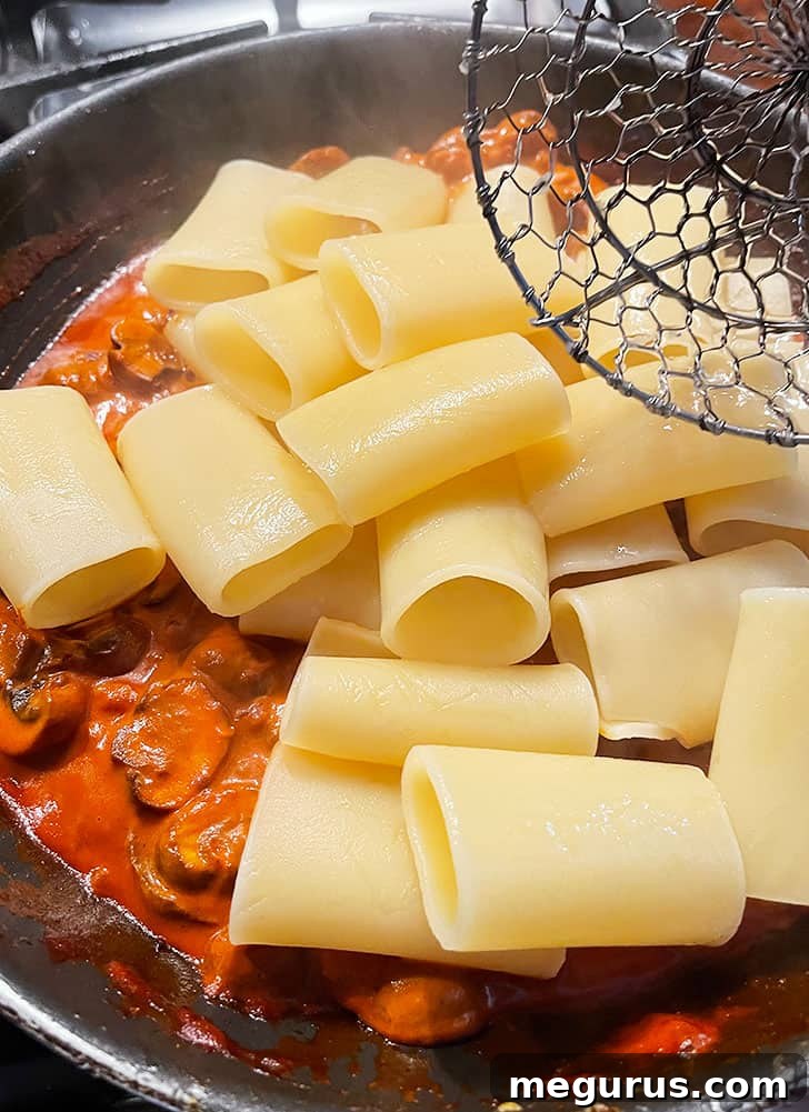 Al dente cooked pasta being transferred directly into the pan with the mushroom ragù