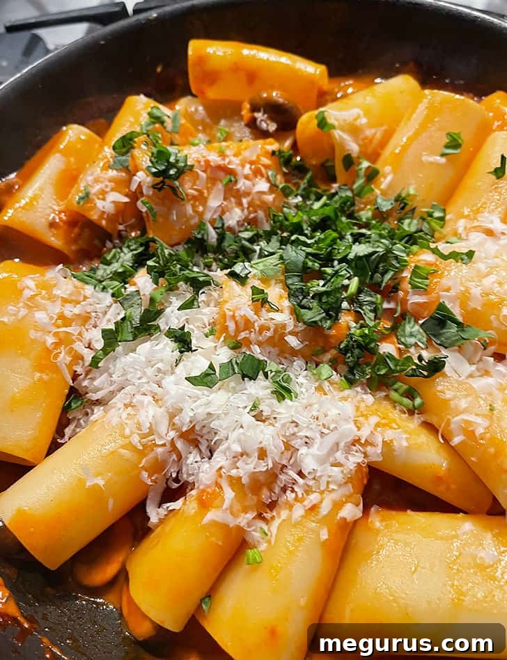 Grated Parmesan cheese and fresh basil being stirred into the pasta and ragù