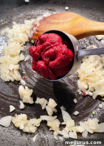 Sautéed onion, garlic, and red pepper flakes with tomato paste browning in a pan