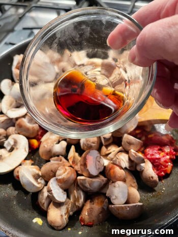 Sliced mushrooms and Marsala wine being added to the pan with sautéed aromatics and tomato paste