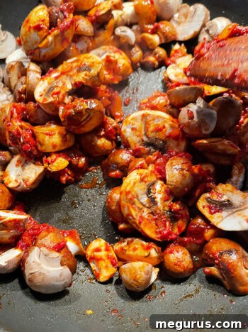 Mushrooms cooking and softening in the pan with the ragù base, stirred occasionally
