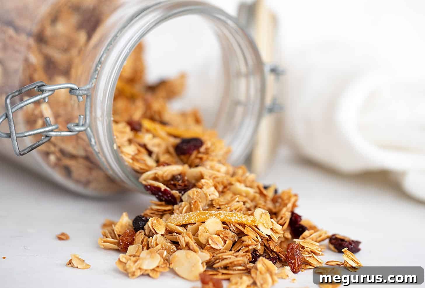 Close-up of vibrant cranberry orange granola spilling from a glass jar, showcasing crispy oats, juicy cranberries, and bright orange peel.