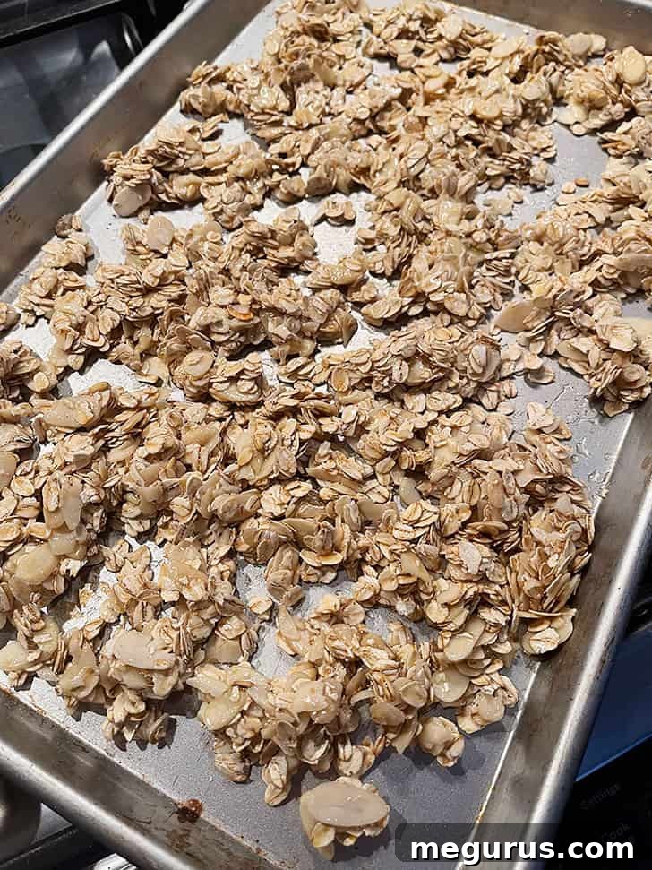 The honey-coated granola mixture spread thinly and uniformly on a nonstick baking sheet.