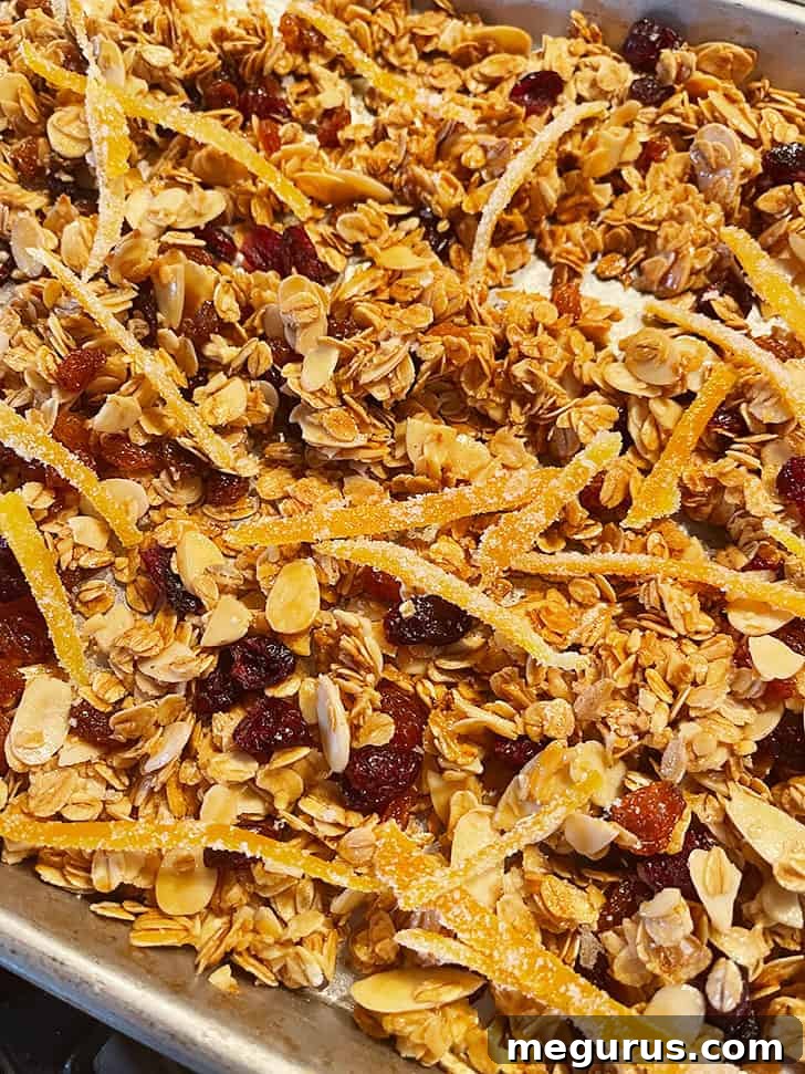The fully baked cranberry orange granola cooling on a baking sheet, ready for final additions.