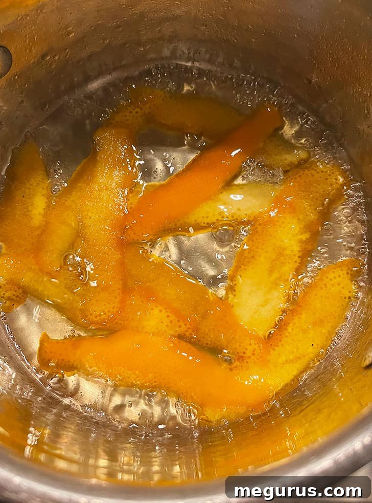 Orange peel simmering gently in a clear sugar syrup on the stovetop.