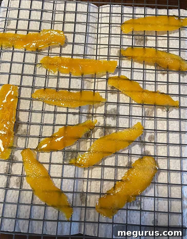 Boiled orange peel strips cooling on a wire rack after being removed from the syrup.