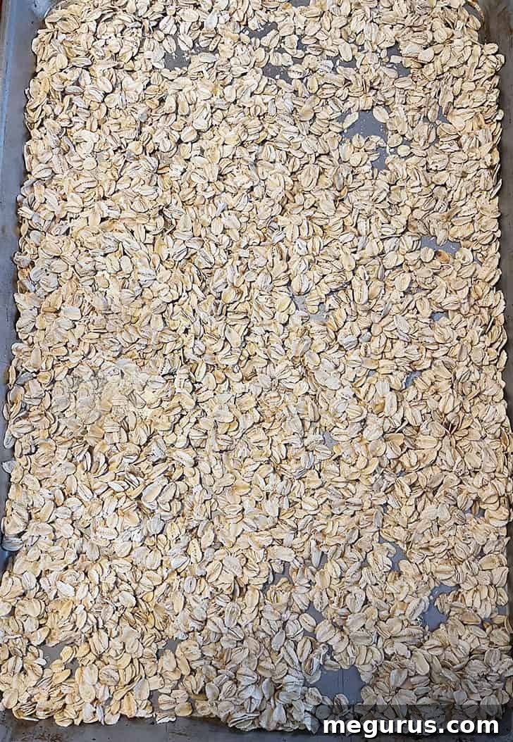 Rolled oats spread evenly on a baking sheet, pre-toasting in the oven to enhance flavor.