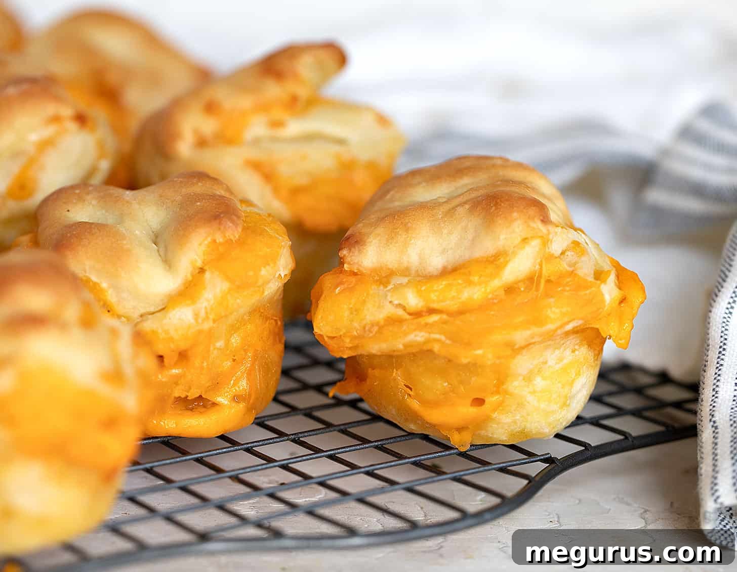 Golden brown cheese buns cooling on a wire rack, showcasing their fluffy texture and melted cheese.