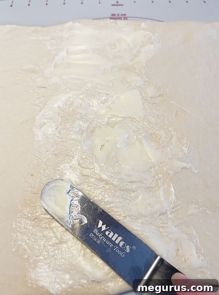 Softened butter being spread evenly onto a section of the rolled-out dough.