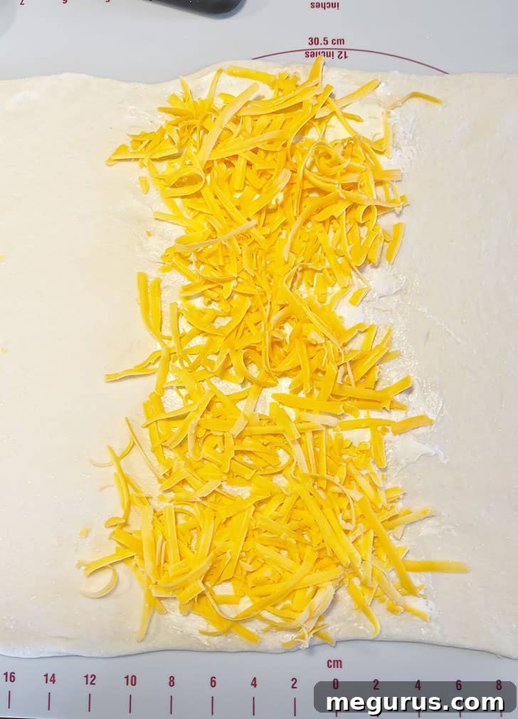 Shredded cheddar cheese being sprinkled over the buttered section of the dough.