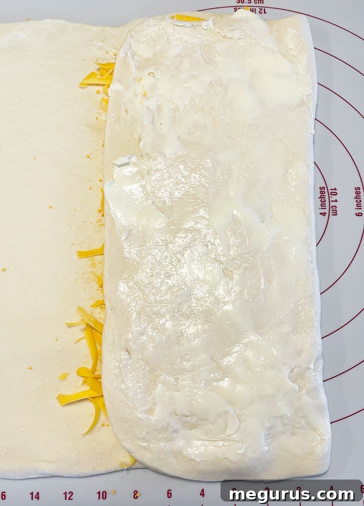 Additional shredded cheese and cheese powder being sprinkled over the second buttered layer.