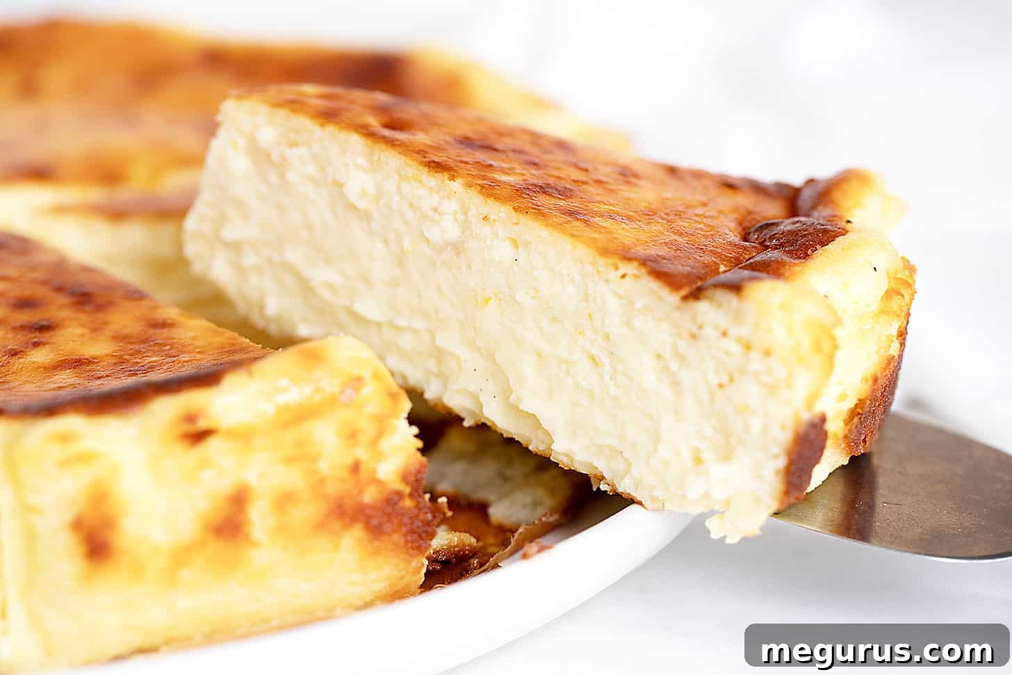 Delightful slice of Lemon Basque Cheesecake on a white plate, showcasing its creamy texture and signature burnt top