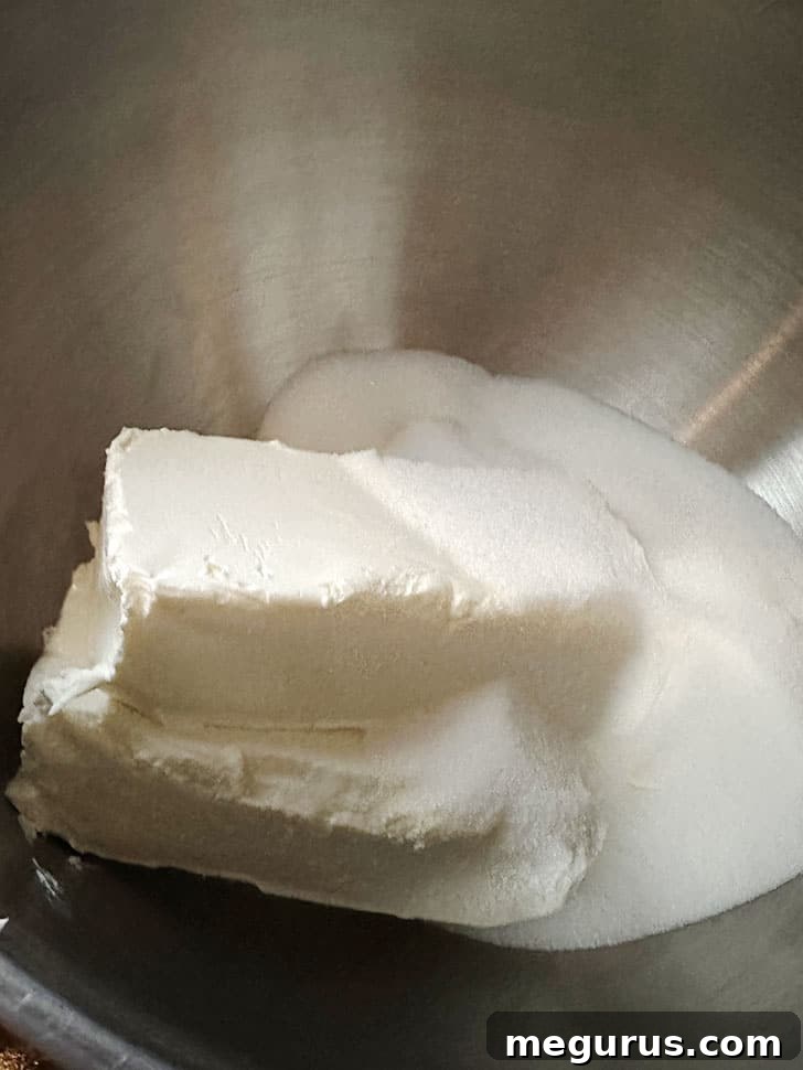 Cream cheese and sugar being mixed in a bowl until smooth.