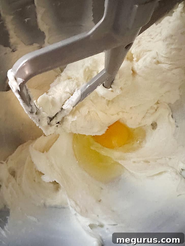 Adding eggs one by one to the cream cheese mixture.