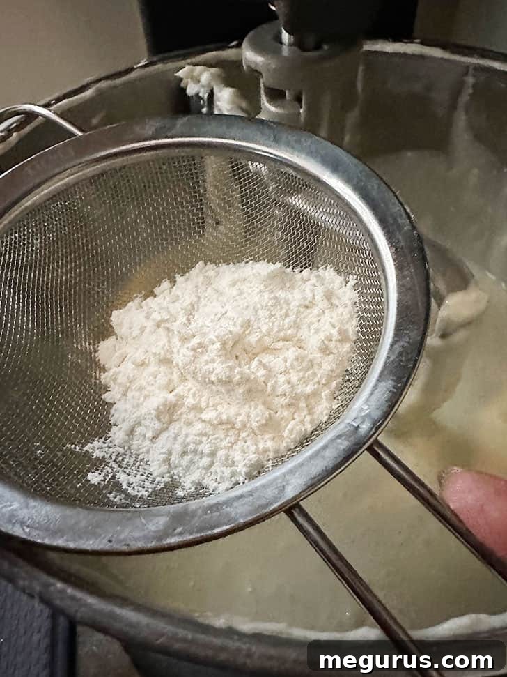 Sifting all-purpose flour into the cheesecake batter.