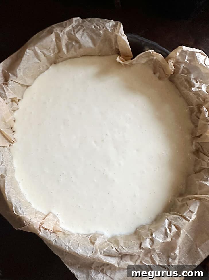 Cheesecake batter poured into a parchment-lined springform pan, ready for the oven.