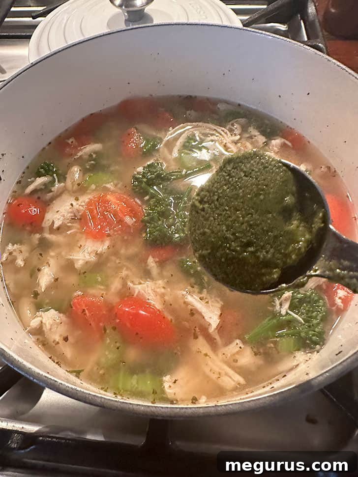 Stirring in fresh basil pesto into the finished chicken and vegetable soup.