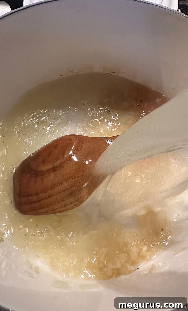 Pouring chicken broth into the pot with sautéed onions and garlic.
