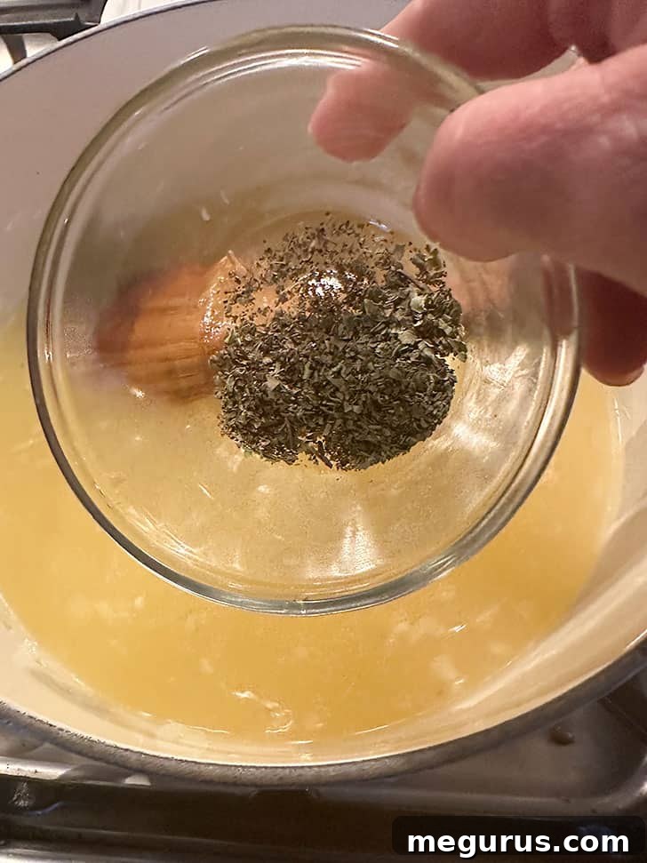 Adding dried oregano and marjoram to the simmering chicken broth.