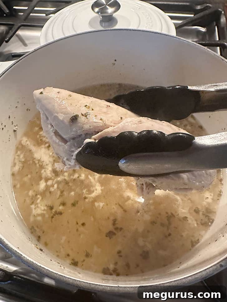 Carefully removing the cooked chicken breast from the pot of broth with tongs.