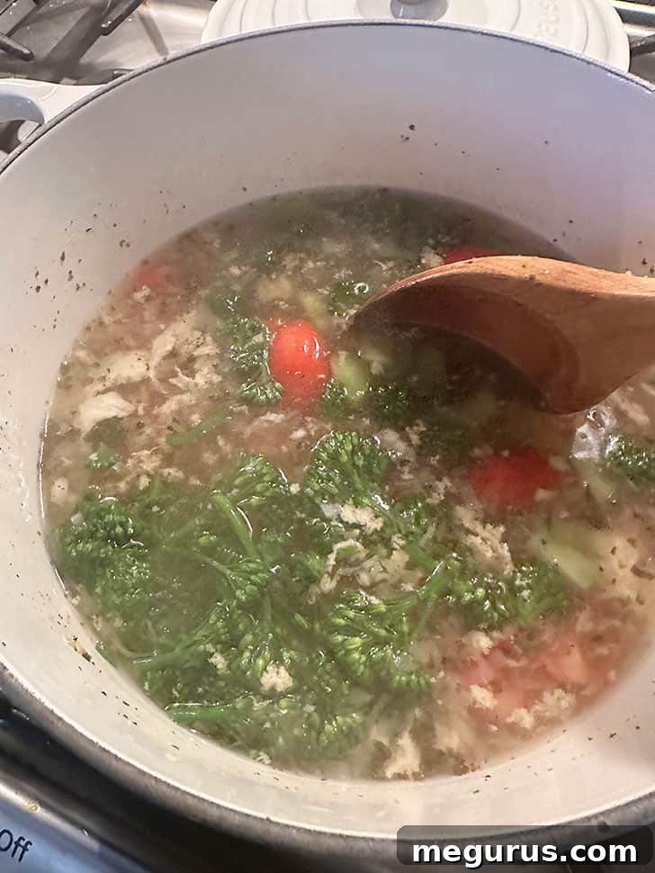 Adding halved cherry tomatoes, thinly sliced celery, and cut broccolini to the hot broth.