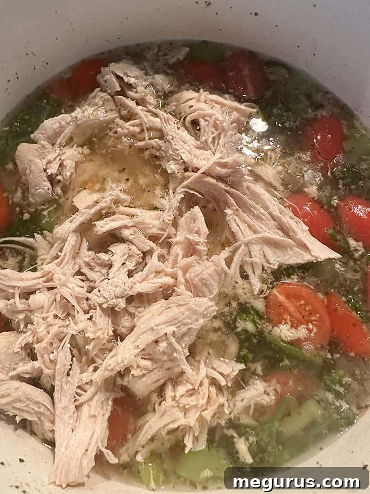 Returning the shredded, cooked chicken to the pot of simmering soup with vegetables.