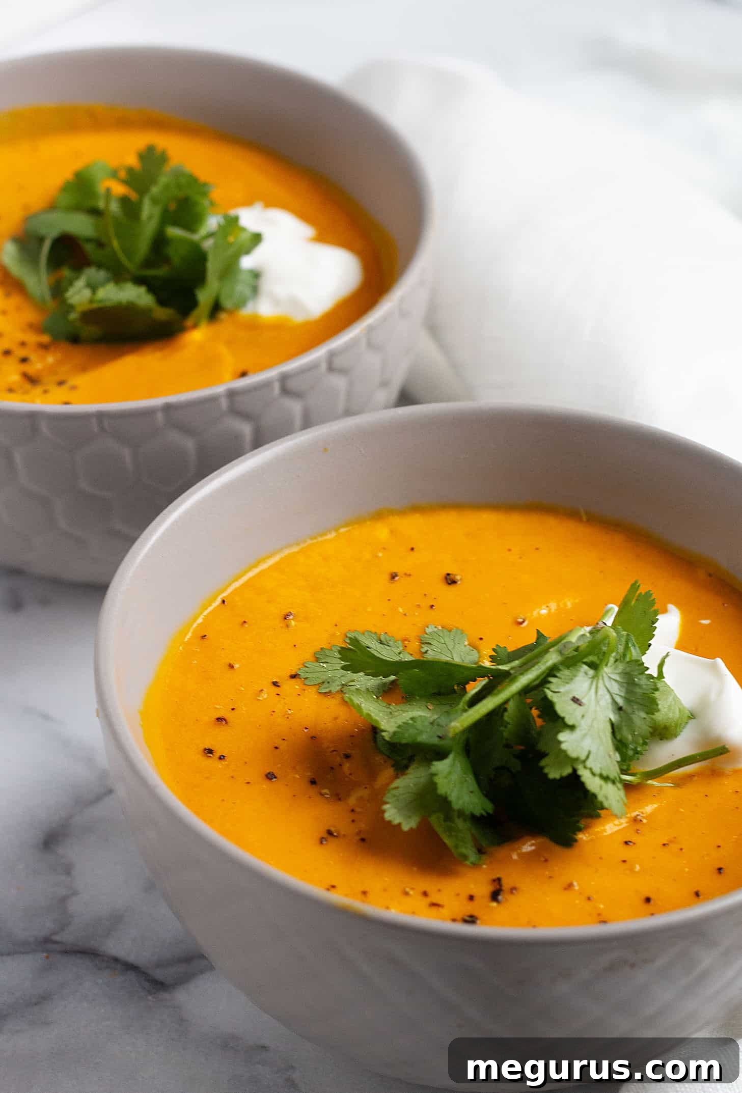 Close-up shot of the rich, orange Thai carrot and pumpkin soup in a ceramic bowl, showcasing its creamy texture and vibrant color.